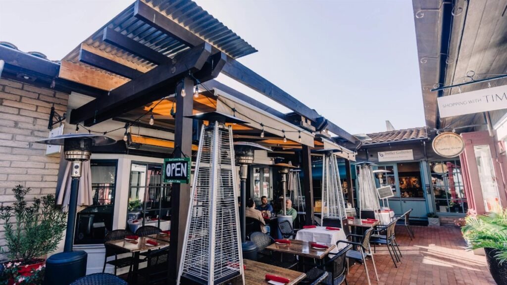 Sunny outdoor restaurant setting with tables, chairs, and heaters under a modern pergola.