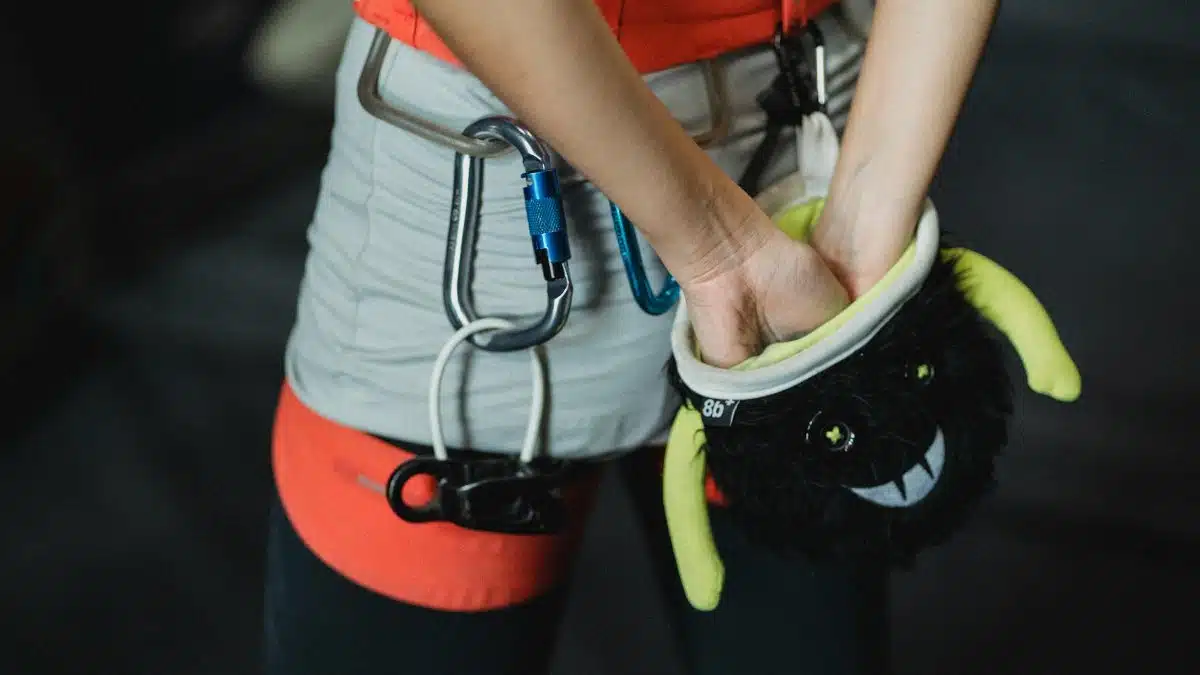 Back view of crop anonymous female climber in protective gear rubbing hands with chalk powder from bag before training in gym