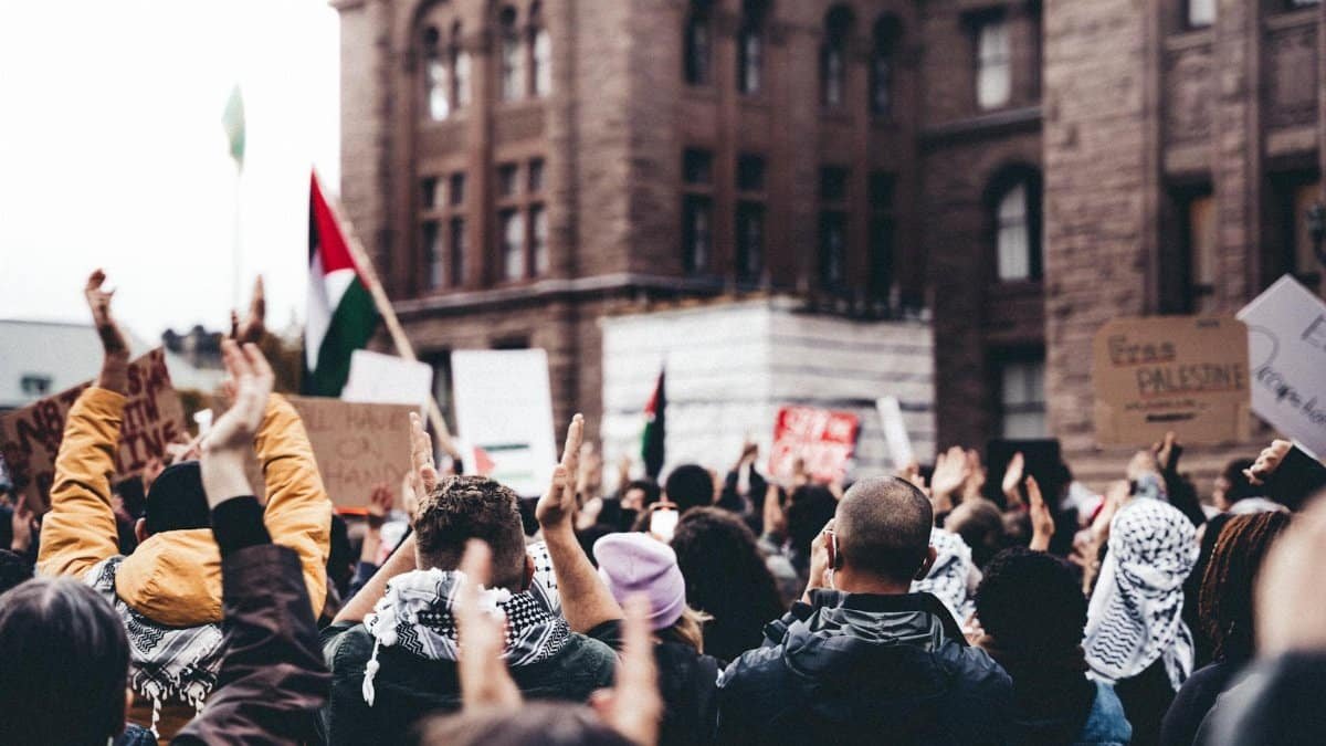 Diverse crowd holding signs and flags during an urban protest, showcasing unity and activism.