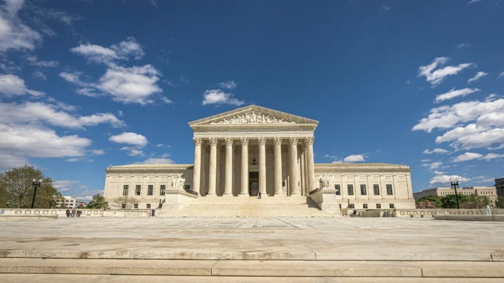 Front view of the United States Supreme Court building on a sunny day with blue sky and clouds.