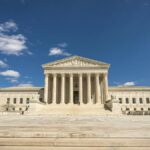 Front view of the United States Supreme Court building on a sunny day with blue sky and clouds.
