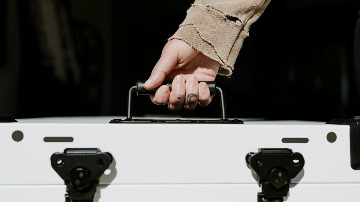 Close-up of a hand carrying a sturdy white case with secure black locks, symbolizing durability.