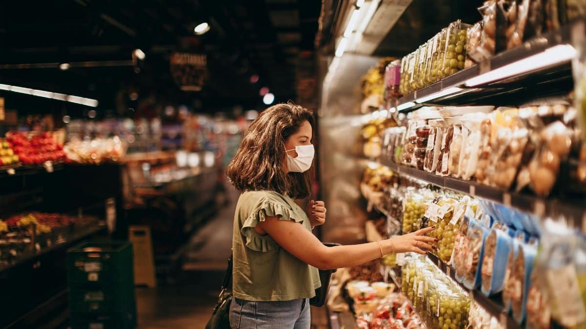 A woman wearing a mask shops for groceries in a supermarket aisle.