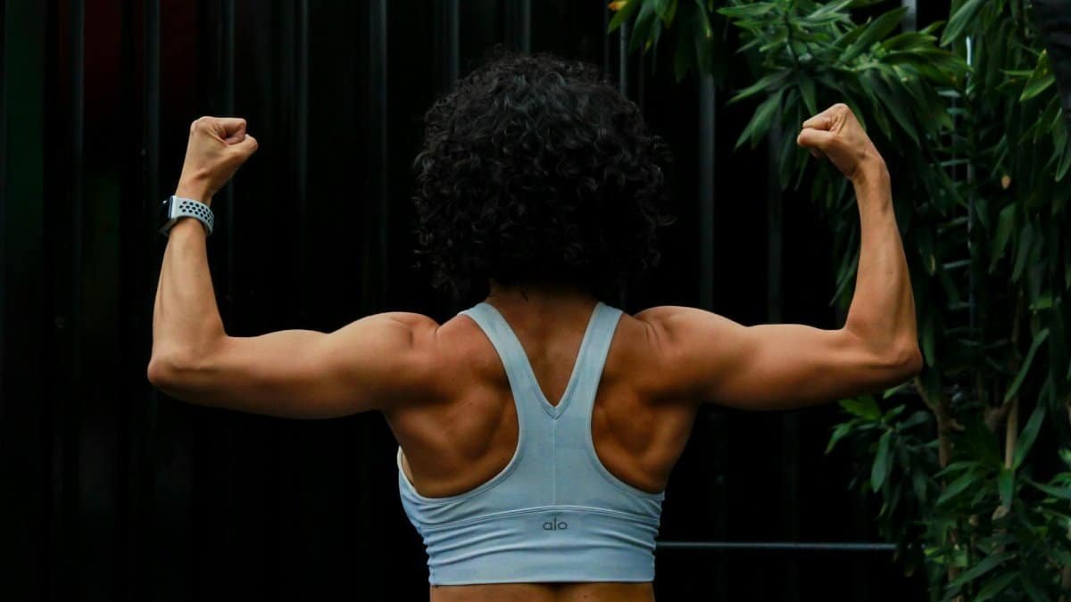 Back view of a muscular woman flexing in a sports bra, demonstrating strength and fitness.