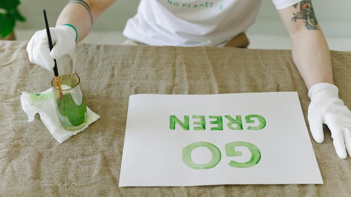 Person painting eco-friendly 'Go Green' message on paper with gloves and brush.