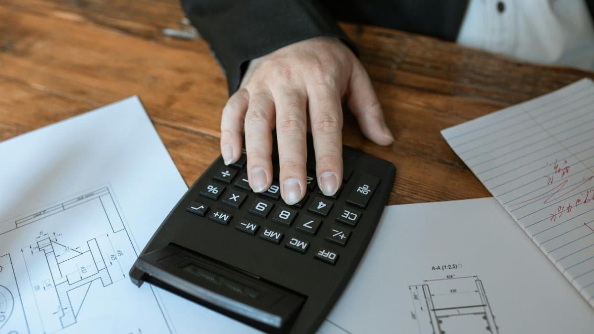 Hand using calculator for architectural calculations on blueprints.