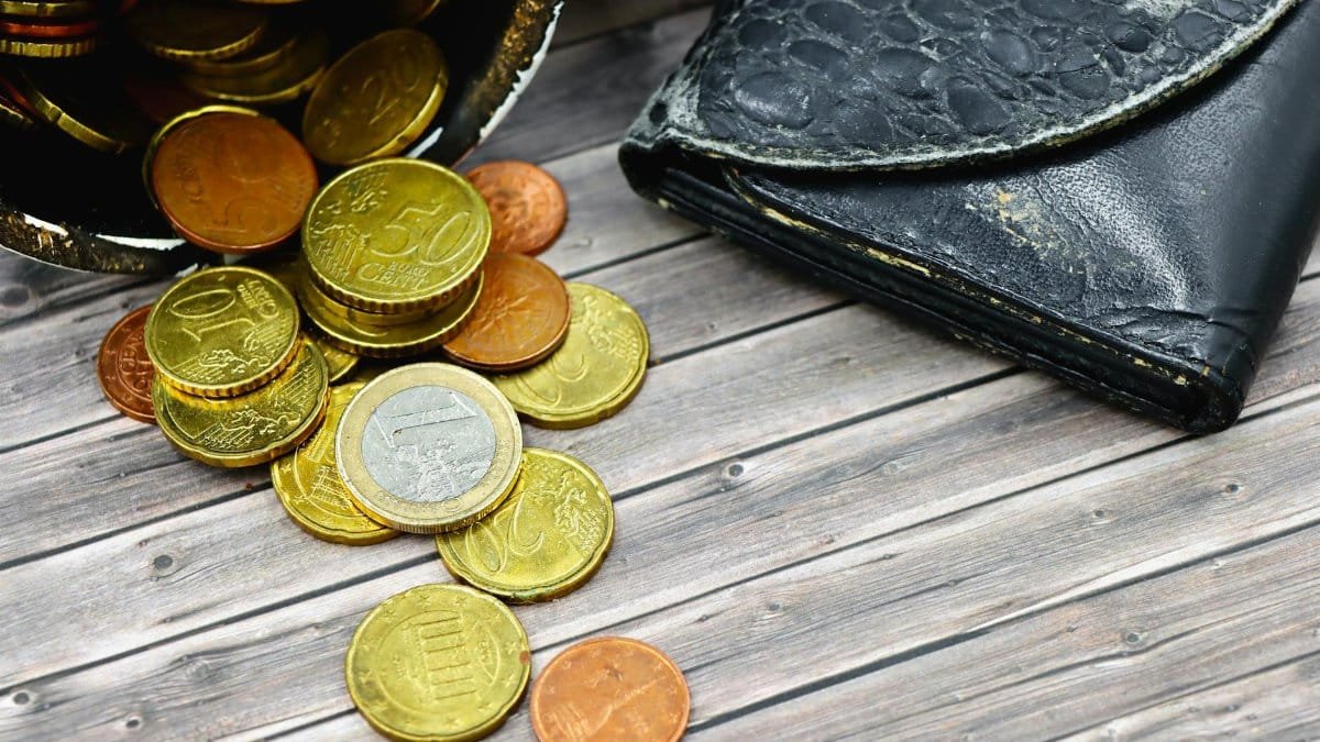 A worn-out leather wallet and scattered euro coins on wooden surface suggest economic hardship.