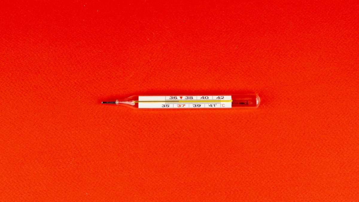 Glass mercury thermometer on a bright red surface, symbolizing health and fever measurement.