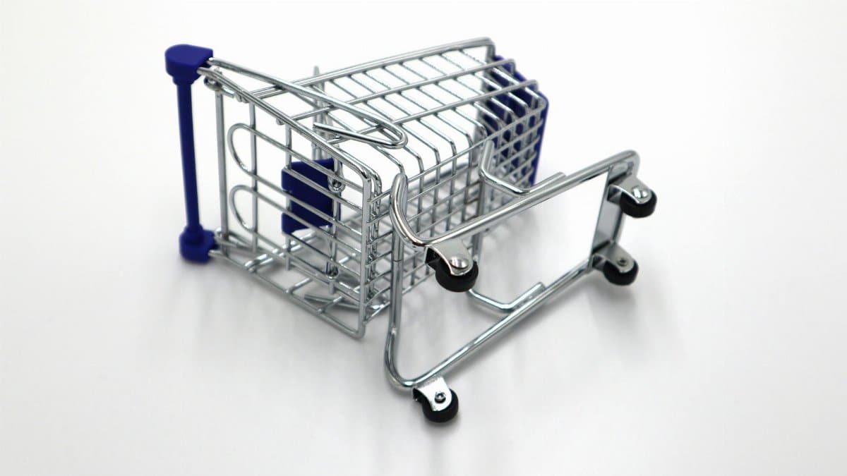 A flipped miniature shopping cart on a white surface symbolizes retail challenges and economic concepts.
