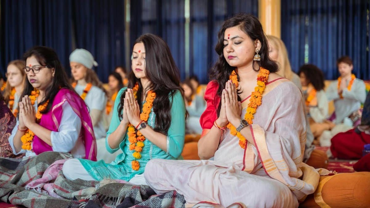 Women meditating in traditional clothing during a spiritual ceremony in Rishikesh, India.