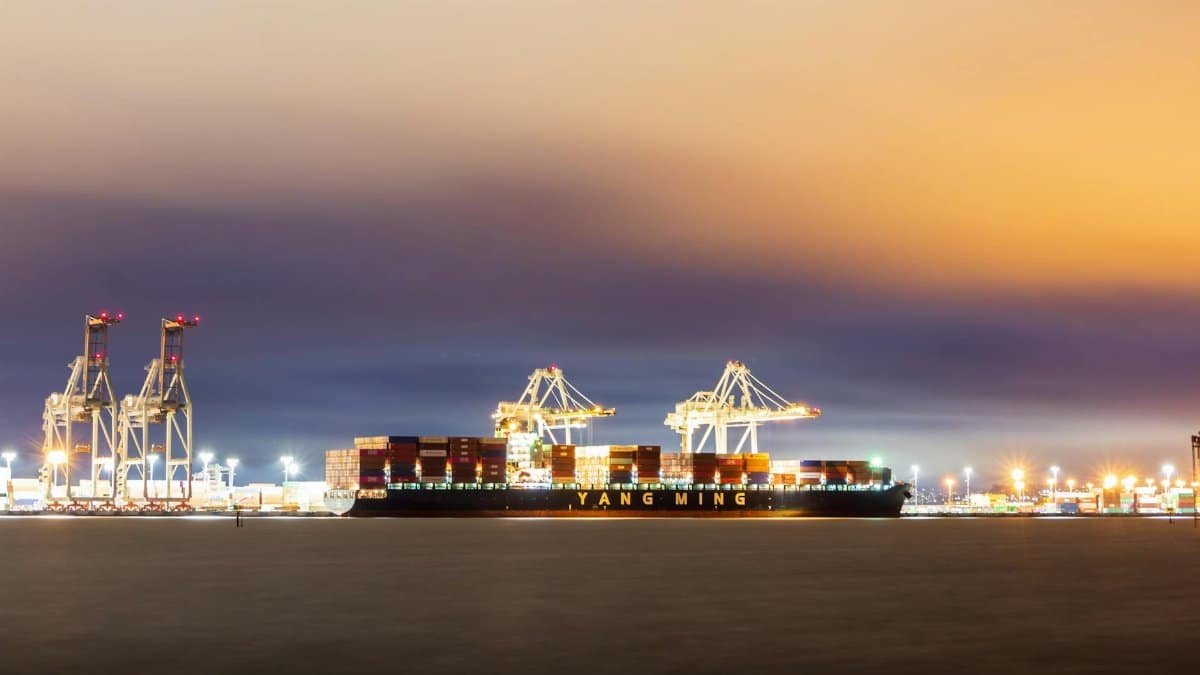 A cargo ship docked in Oakland harbor at sunset with vibrant skies and industrial cranes.