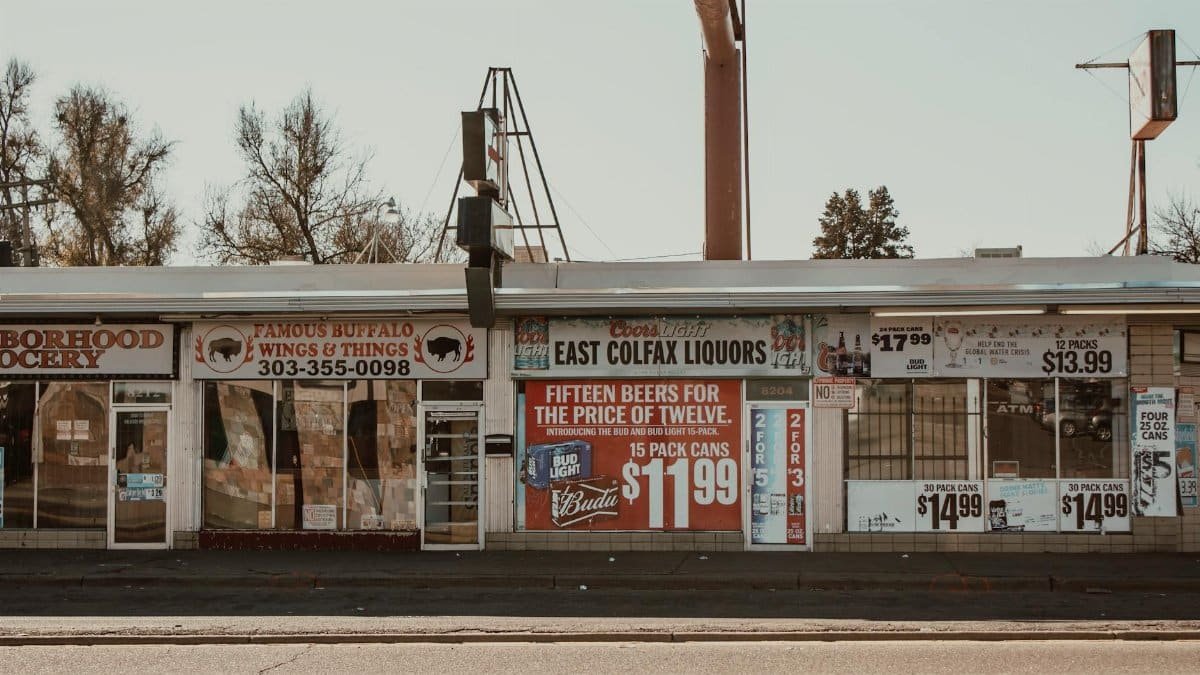 Vintage neighborhood liquor store and grocery with multiple signages on a sunny day.