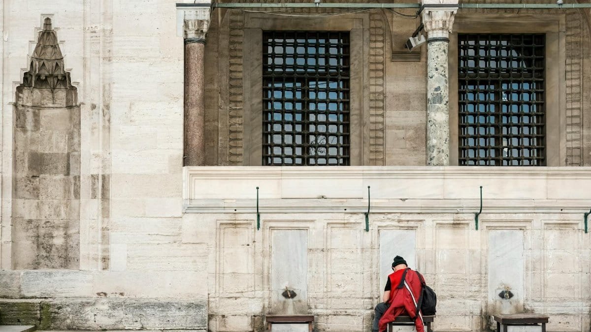 A solitary man performs ablution at an outdoor mosque fountain, emphasizing cultural tradition.