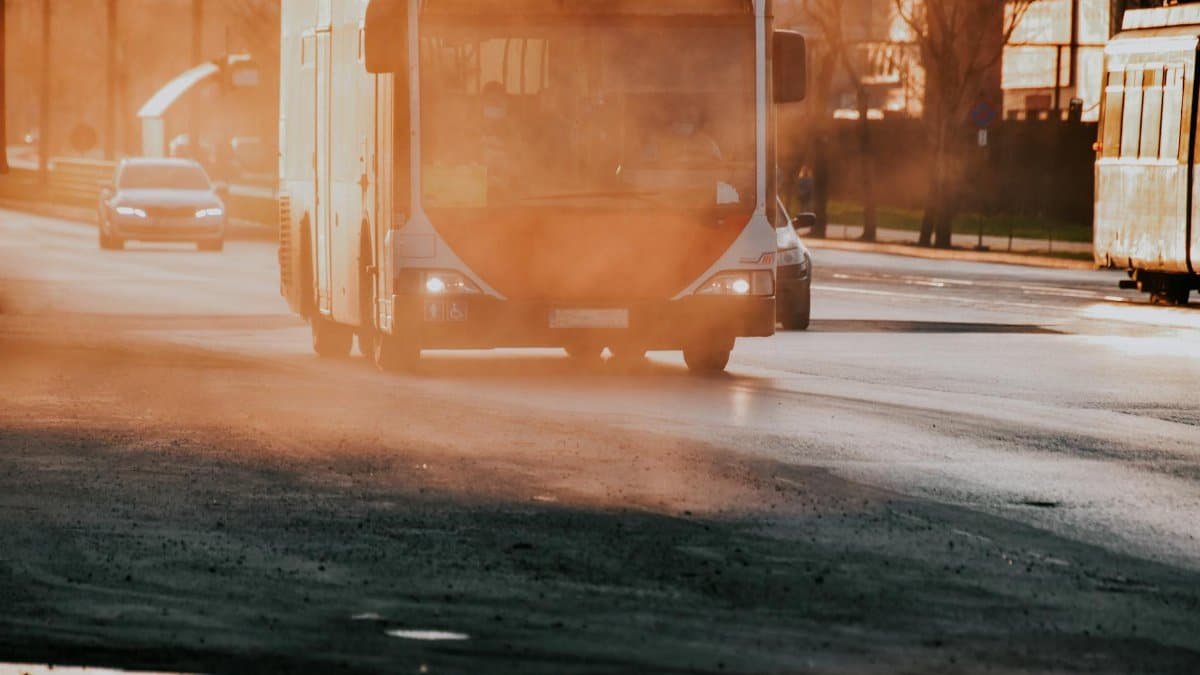 A city bus driving through a dusty street during the morning light, capturing urban life and transportation.