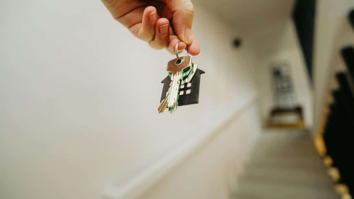 Close-up of a hand holding a keychain in the shape of a house, symbolizing real estate and property ownership.