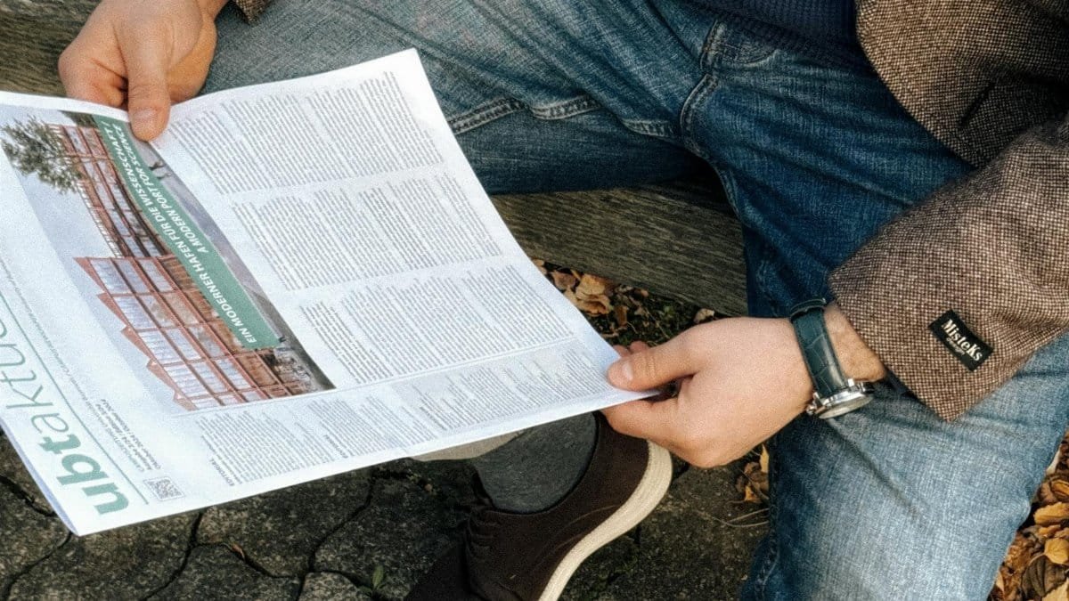 Casually dressed man reading a newspaper outdoors on a park bench in Bayreuth, Germany.