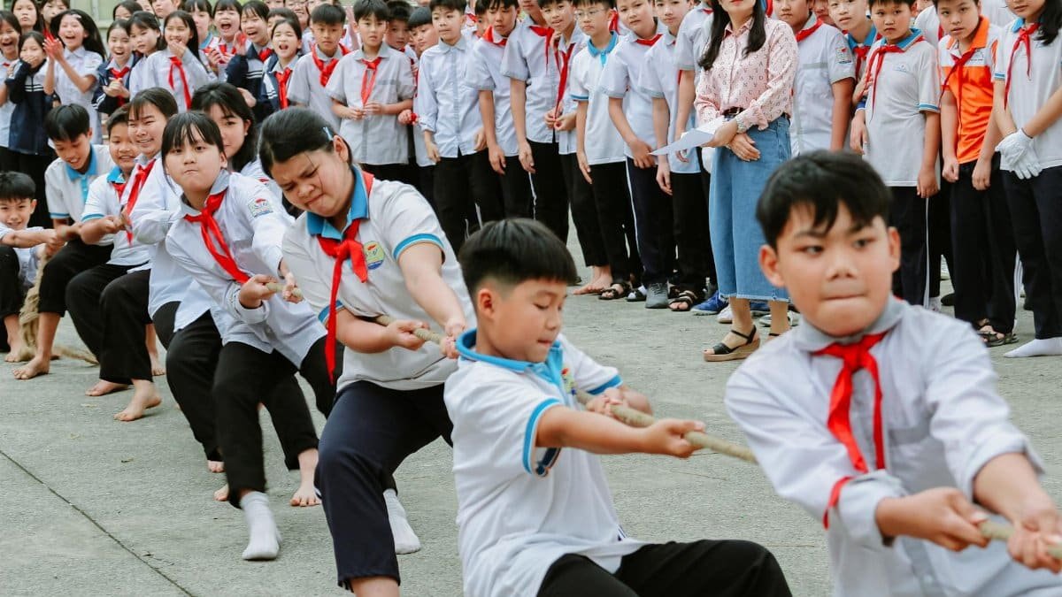 Group of children playing a tug-of-war game outdoors, with their peers watching.