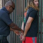 Police officer handcuffing a suspect during an arrest against an urban backdrop.