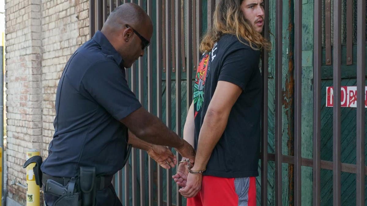 Police officer handcuffing a suspect during an arrest against an urban backdrop.