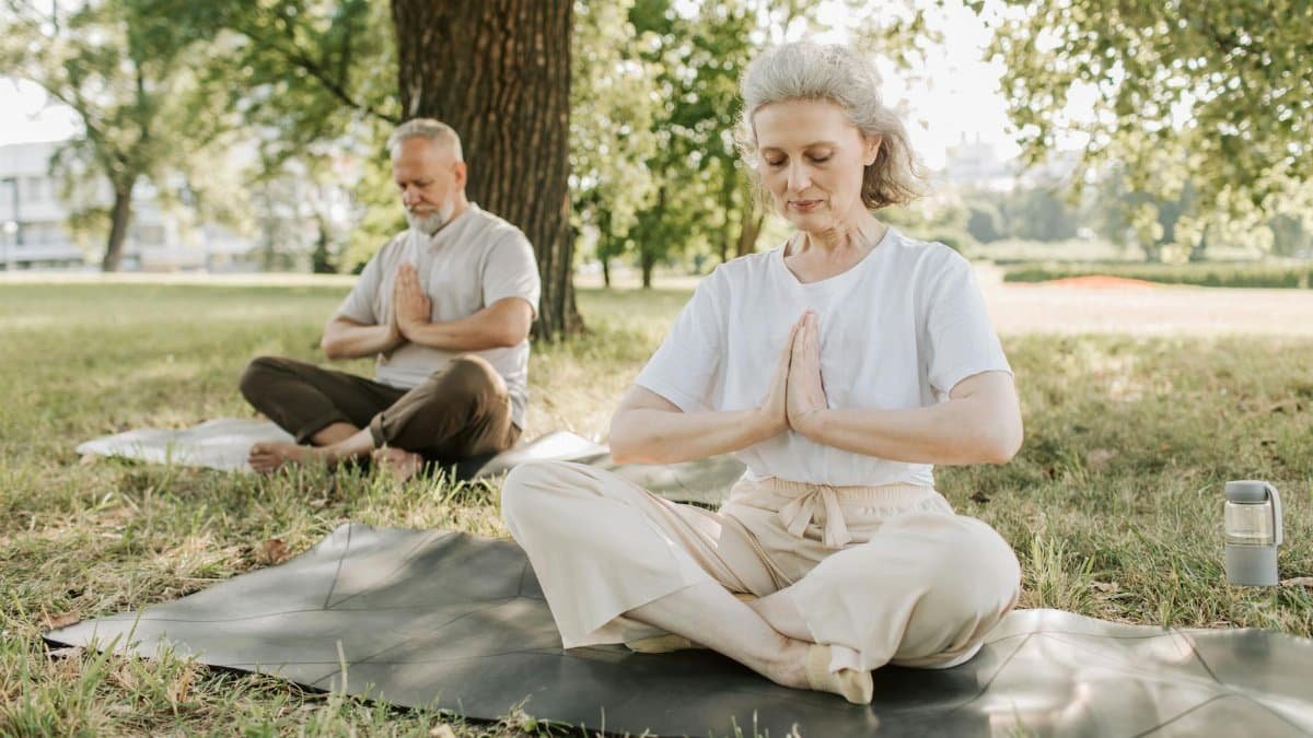 Elderly couple practicing yoga meditation outdoors, focusing on health and tranquility.
