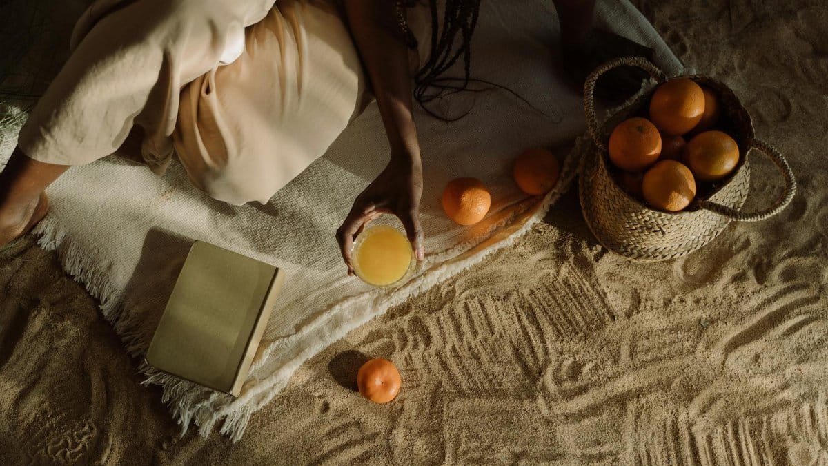Serene beach scene with a woman enjoying a picnic with oranges and juice.