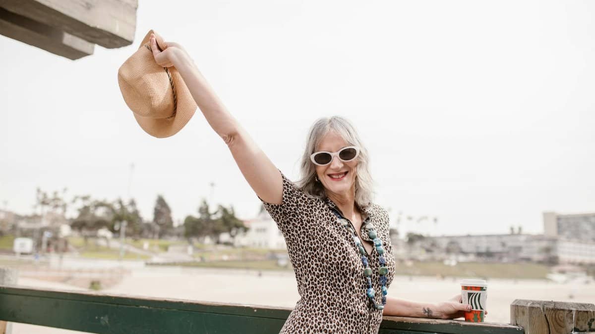 Stylish senior woman with hat at the beach, embracing life joyfully.