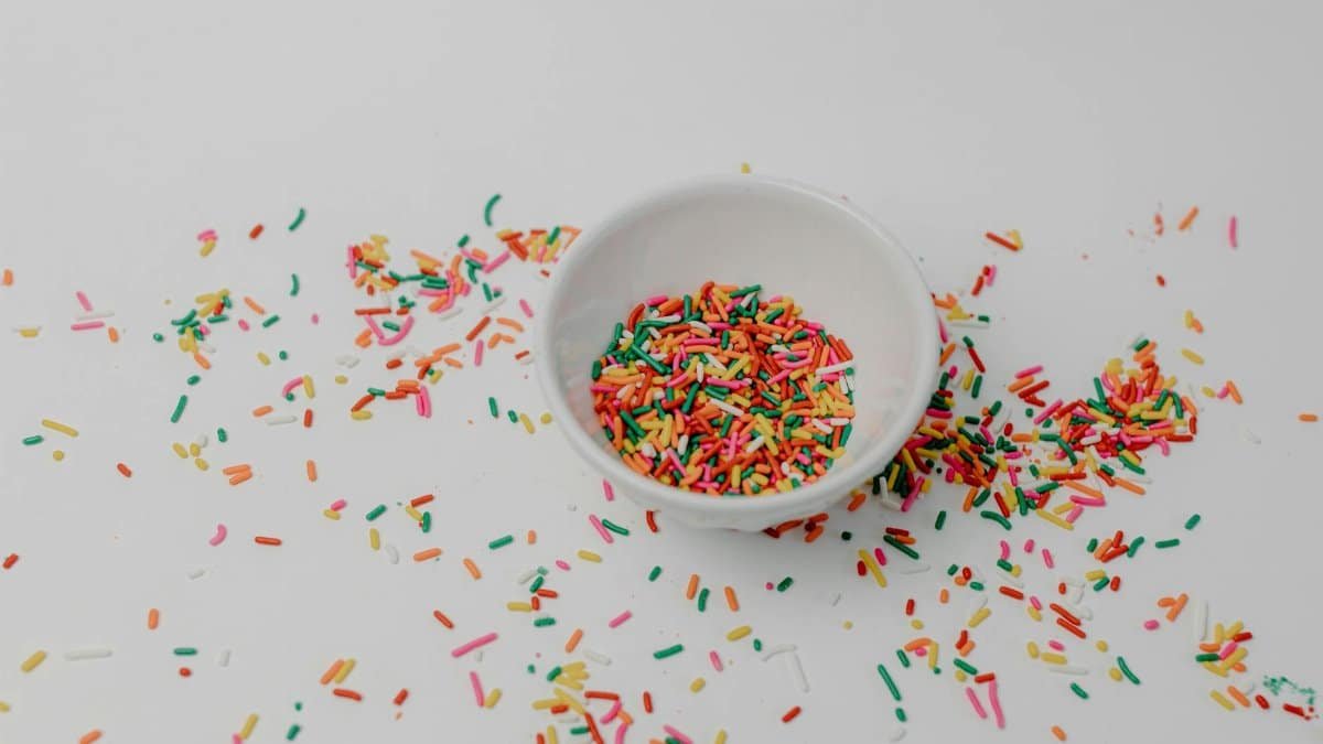 Vibrant rainbow sprinkles scattered around a white ceramic bowl, creating a playful and sweet still life arrangement.