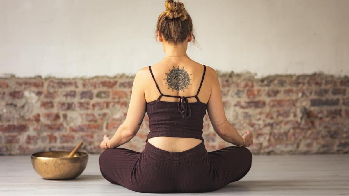 Woman meditating indoors with a tattoo on her back, embracing peace and zen.