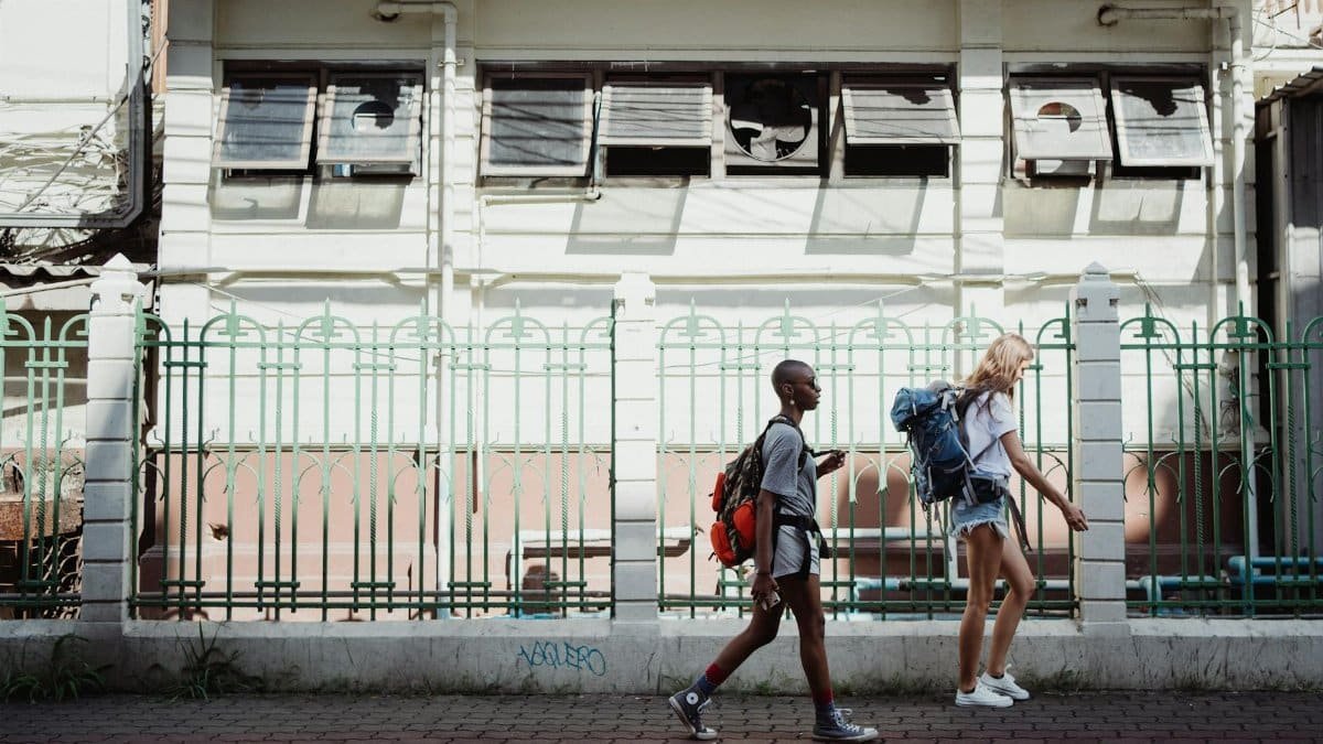 Two women walking with backpacks on a city sidewalk, embracing urban exploration.
