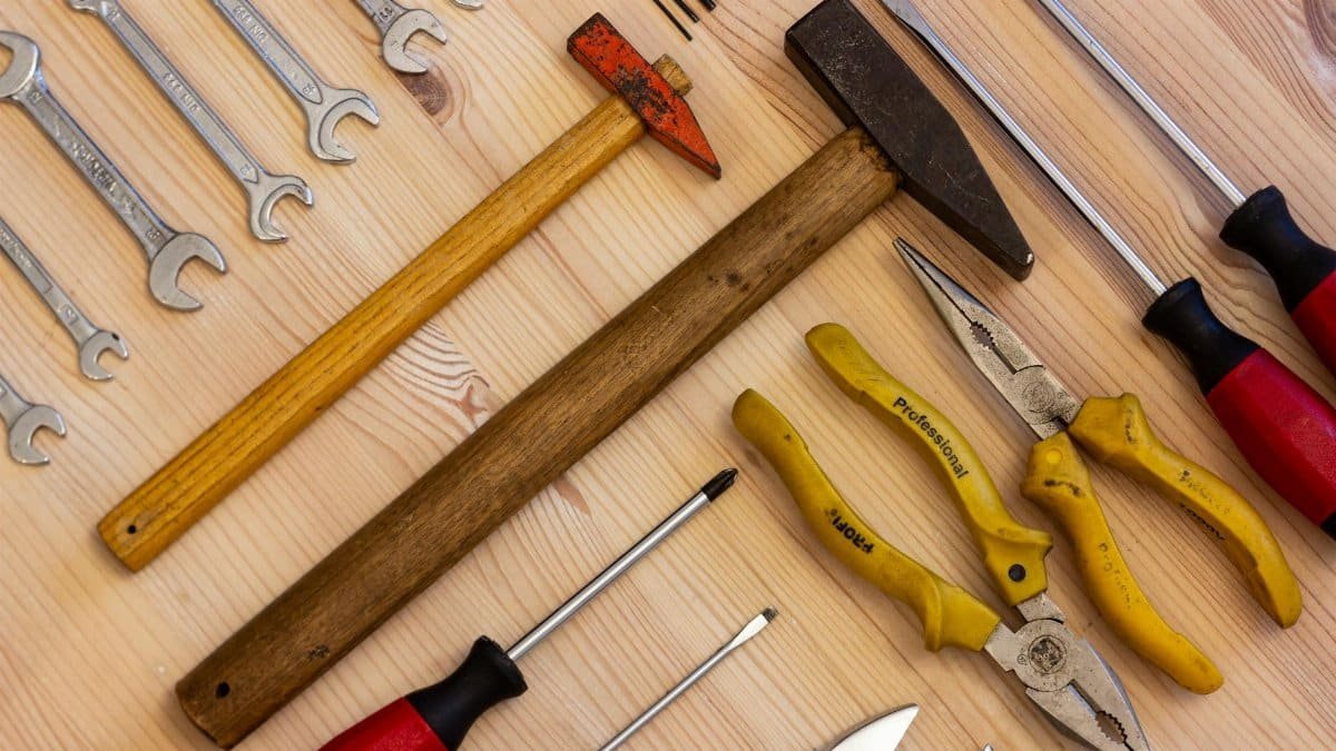 A variety of hand tools including wrenches, screwdrivers, and pliers on a wooden surface.