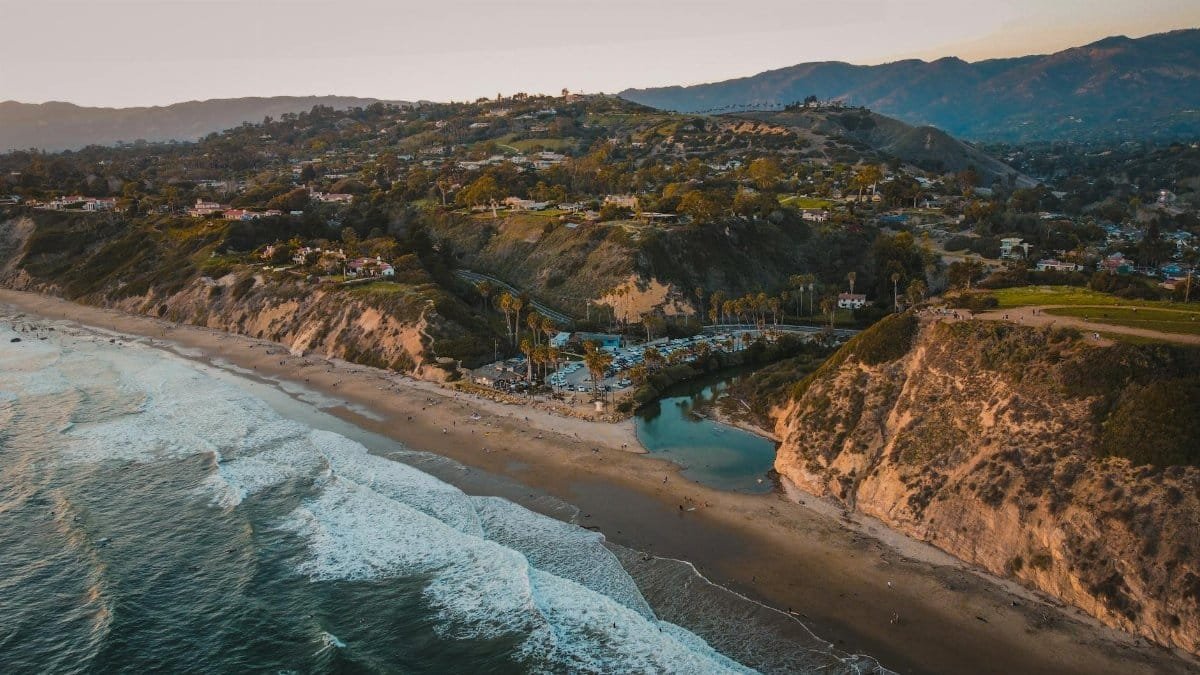Breathtaking aerial view of Santa Barbara's coastline with waves crashing on the sandy shore at sunset.