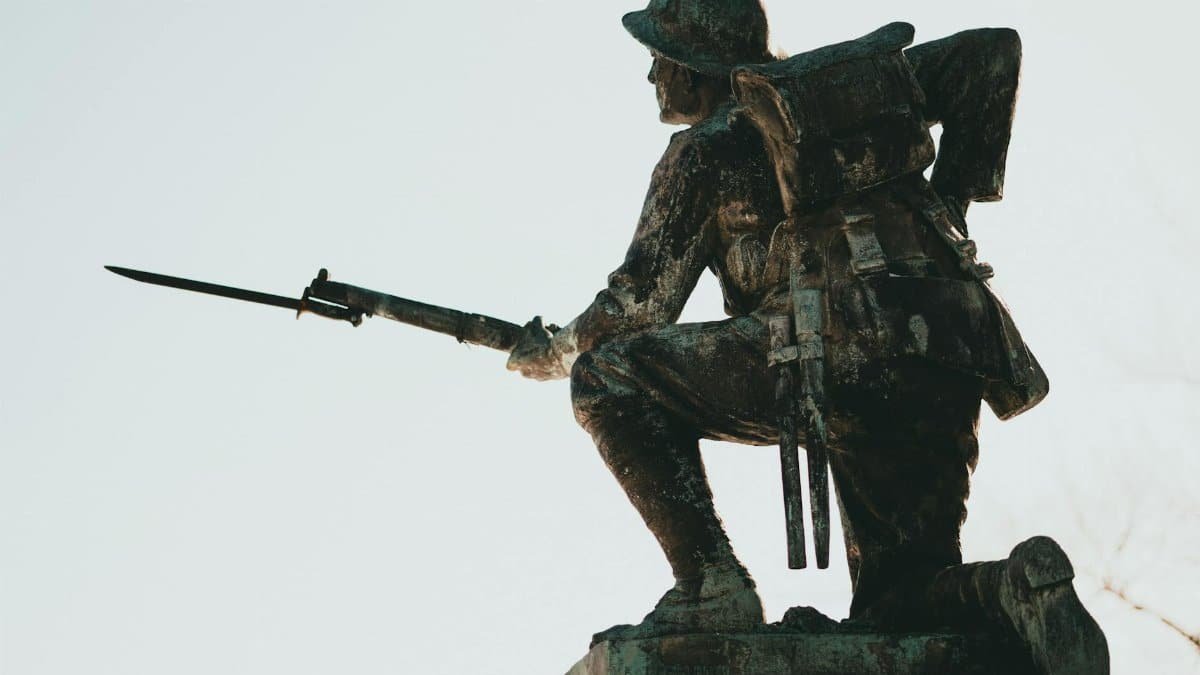 Bronze soldier statue with bayonet, symbolizing military history and valor in sunlight.