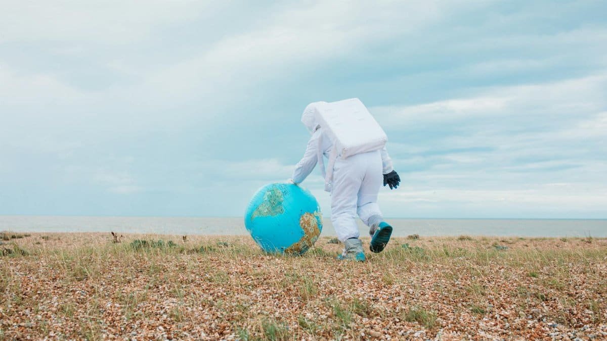 Astronaut in space suit walking on a pebbled beach with an inflatable Earth globe.