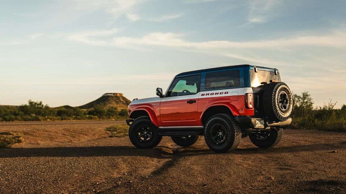A red SUV off-road vehicle parked in a desert with hills in the background during sunset.