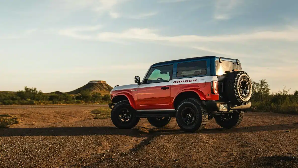 A red SUV off-road vehicle parked in a desert with hills in the background during sunset.