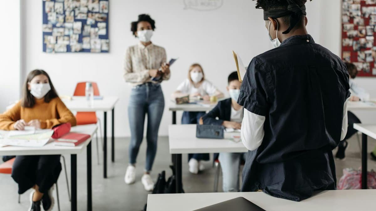 A teacher and students wearing masks in a classroom setting, adapting to new normal education during the pandemic.