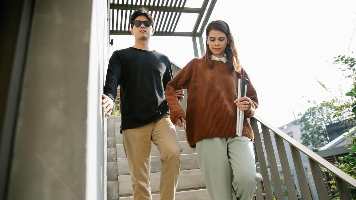 Two young adults walk downstairs with sunlight casting shadows. Casual scene outdoors.