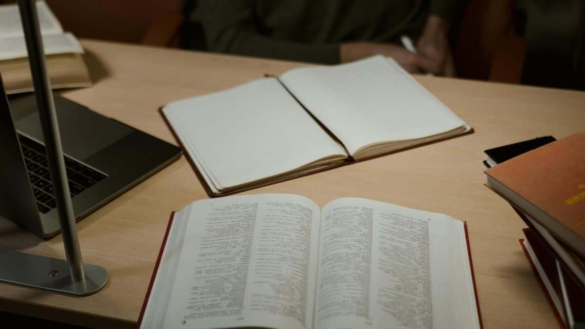 A warm, indoor study setup featuring open books and a laptop on a wooden desk, ideal for research and learning.
