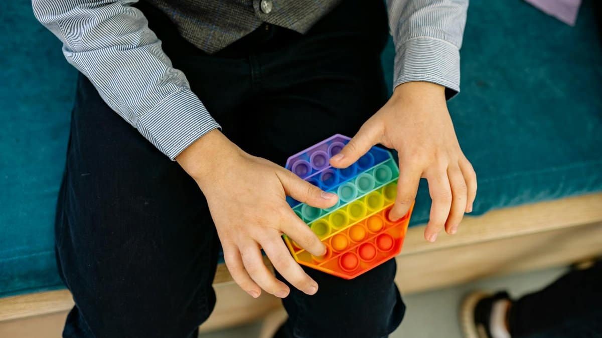 A child's hands engaging with a rainbow pop it fidget toy, promoting sensory play.