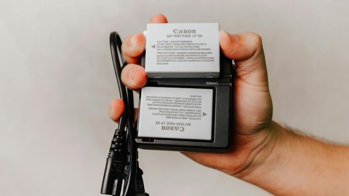 Close-up of a hand holding a Canon battery charger with cables, essential for photography electronics.