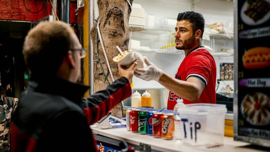 Street vendor serves food to a customer at an outdoor counter, capturing a vibrant city life moment.