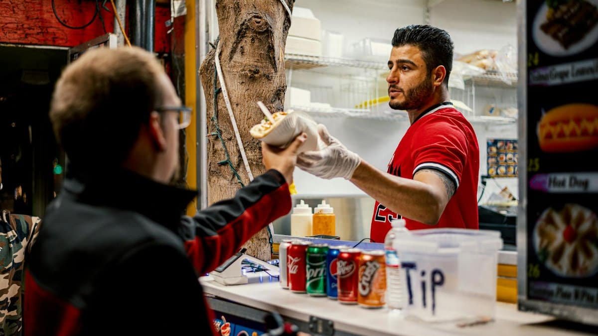 Street vendor serves food to a customer at an outdoor counter, capturing a vibrant city life moment.