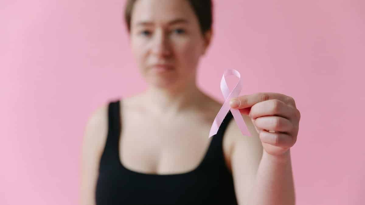 Woman holding a pink ribbon symbolizing breast cancer awareness against a pink background.
