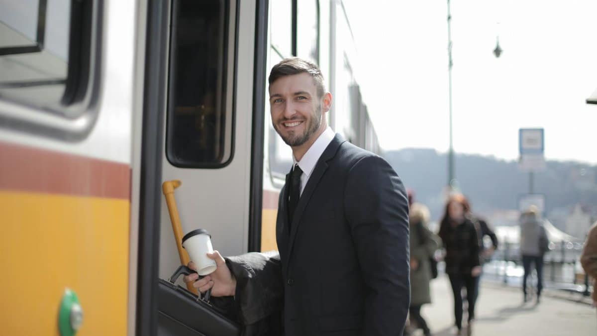 Confident businessman with suitcase and coffee boarding train during daily commute.