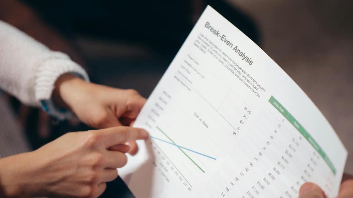 Close-up of hands discussing a break-even analysis document in a business meeting.