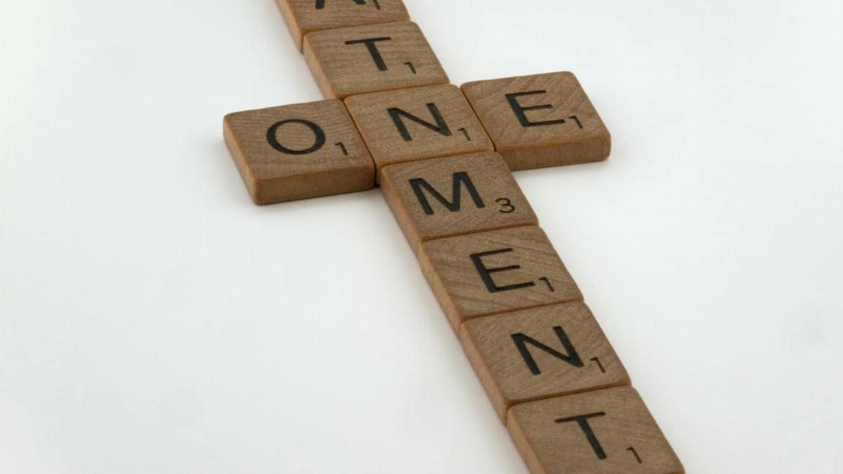 Scrabble tiles arranged in a cross shape spelling 'atonement' on a white background.