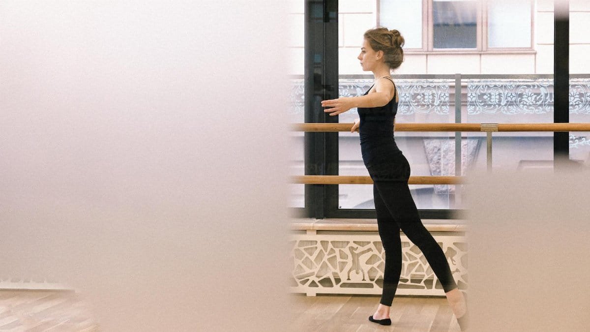 A focused ballerina practicing her dance technique at the barre in a ballet studio.