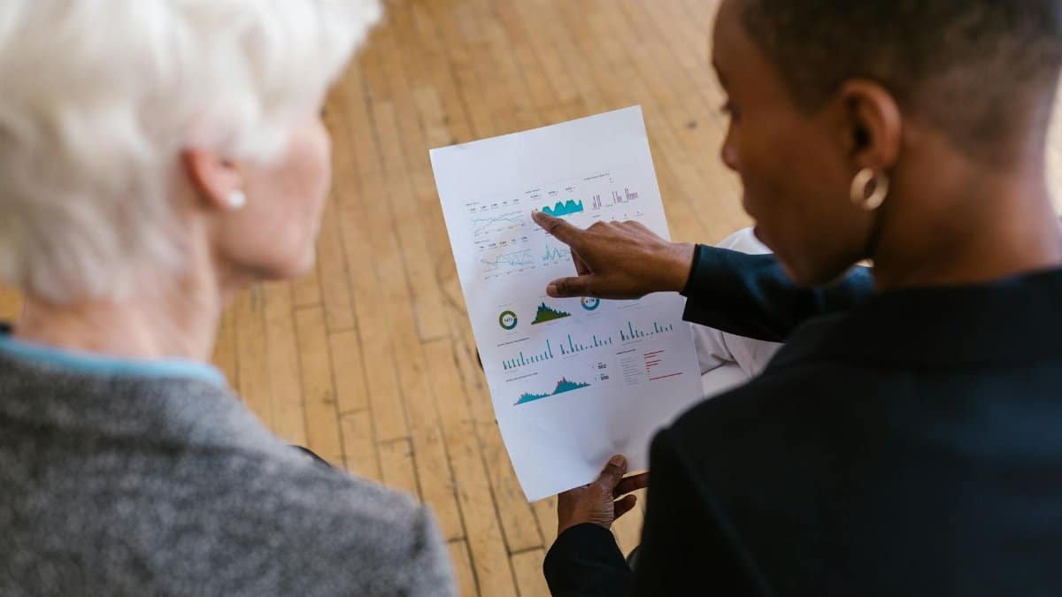 Two professionals reviewing business documents with graphs in an office setting.