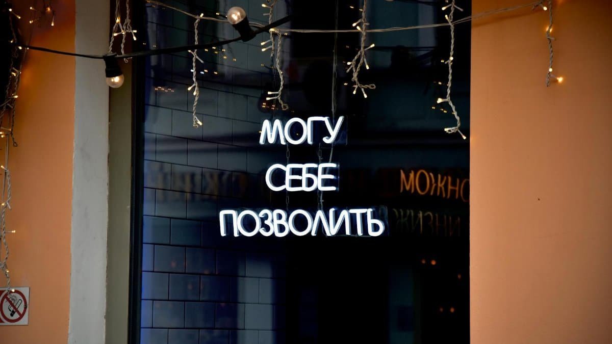 Neon sign in Russian with decorative string lights at night.