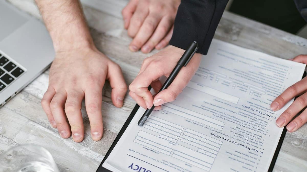Close-up image of two people signing an insurance policy document on a wooden desk.